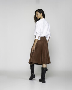 Vista trasera de falda midi marrón con caída amplia y vuelo, combinada con camisa blanca y botas altas negras, modelo Formentera