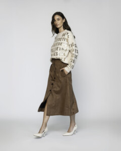 Vista lateral de falda midi camel con abertura delantera abotonada y bolsillos, combinada con suéter oversize estampado
