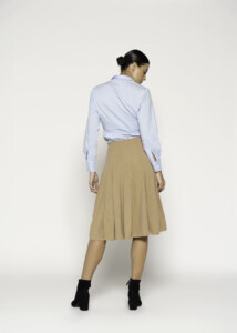 Vista trasera de falda midi camel con pliegues y camisa celeste cruzada en la espalda, combinada con botines negros