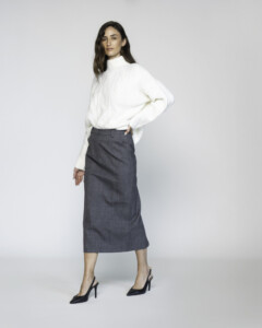 Vista lateral de falda midi gris de corte recto, con cintura alta y textura de lana, combinada con suéter blanco de cuello alto