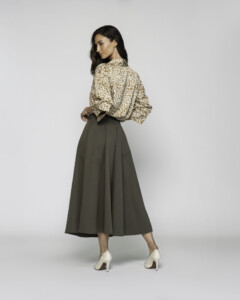 Vista trasera de falda midi verde militar con pliegues, camisa estampada beige anudada en cintura, modelo Formentera