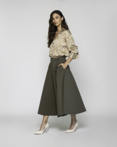 Vista lateral de tres cuartos de falda midi verde militar con pliegues y volumen, combinada con camisa estampada, modelo Formentera