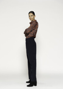 Vista lateral de cuerpo completo mostrando pantalón ancho negro de tiro alto con blusa estampada en tonos naranjas y negros