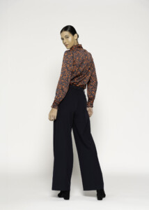 Vista lateral de pantalón negro de tiro alto con pernera ancha, combinado con blusa estampada naranja y negro