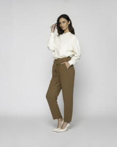 Vista lateral de pantalón camel con cordón, pinzas y bolsillos, combinado con suéter blanco oversize y stilettos crema