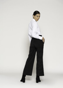 Vista de espalda del pantalón negro con rayas finas, se aprecia el corte ancho y caída recta, con camisa blanca metida