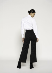 Vista posterior de pantalón negro a rayas con corte ancho, combinado con camisa blanca, se aprecia caída recta y largo crop, modelo Formentera