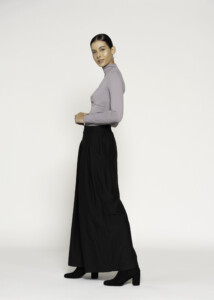 Vista lateral del pantalón palazzo negro de tiro alto con pierna amplia, combinado con top lila de cuello alto modelo Formentera