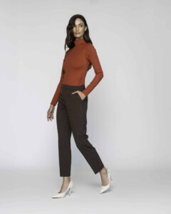 Vista lateral del pantalón recto de cuadros café con blusa teja de cuello alto y mano en bolsillo, modelo Formentera