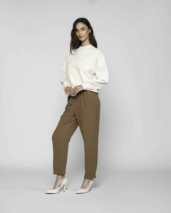 Vista de cuerpo completo del polerón crudo combinado con pantalón camel, modelo luciendo la prenda en pose lateral sobre fondo claro