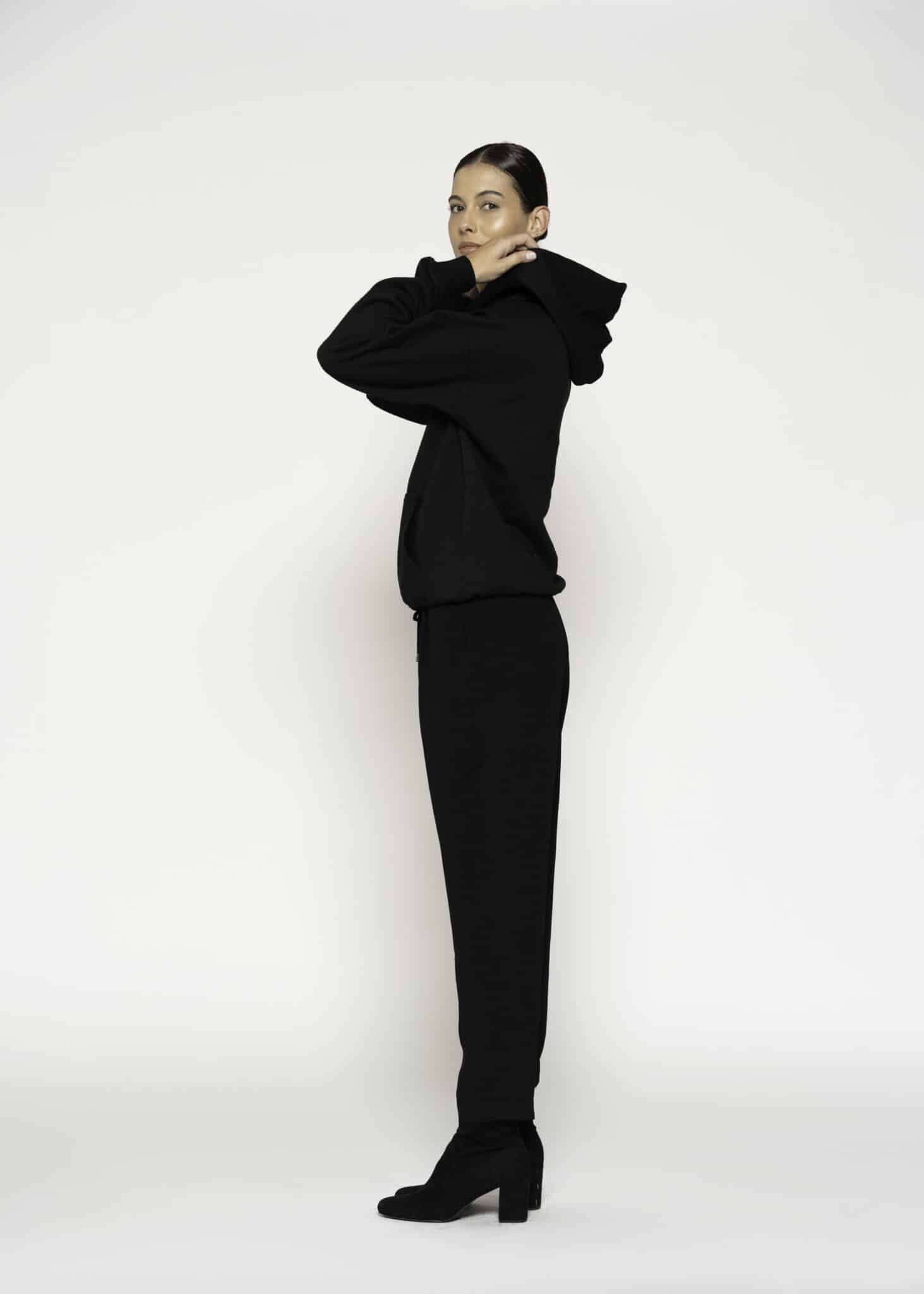 Vista lateral completa de polerón negro oversize con capucha y pantalones a juego, modelo Formentera en postura pensativa