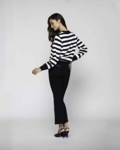 Vista lateral de tres cuartos de sweater a rayas horizontales blancas y negras con puños y cuello negro, combinado con pantalón negro
