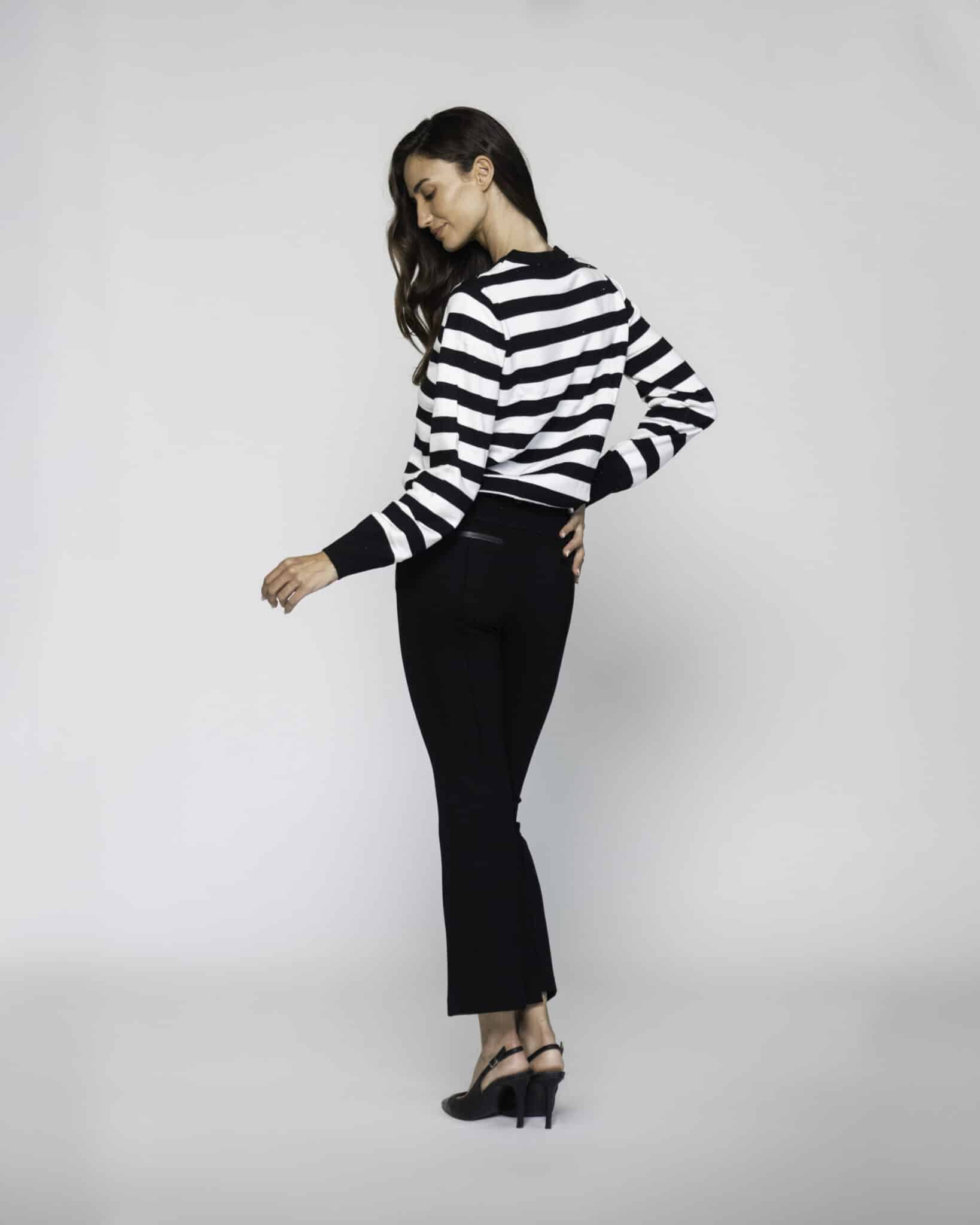 Vista lateral de tres cuartos de sweater a rayas horizontales blancas y negras con puños y cuello negro, combinado con pantalón negro