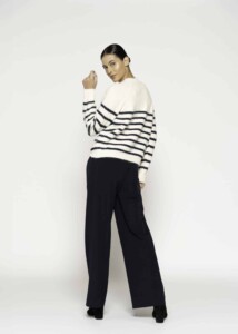 Vista de espalda tres cuartos del sweater tejido a rayas horizontales crudo y azul marino, mostrando caída oversize y pantalones negros amplios
