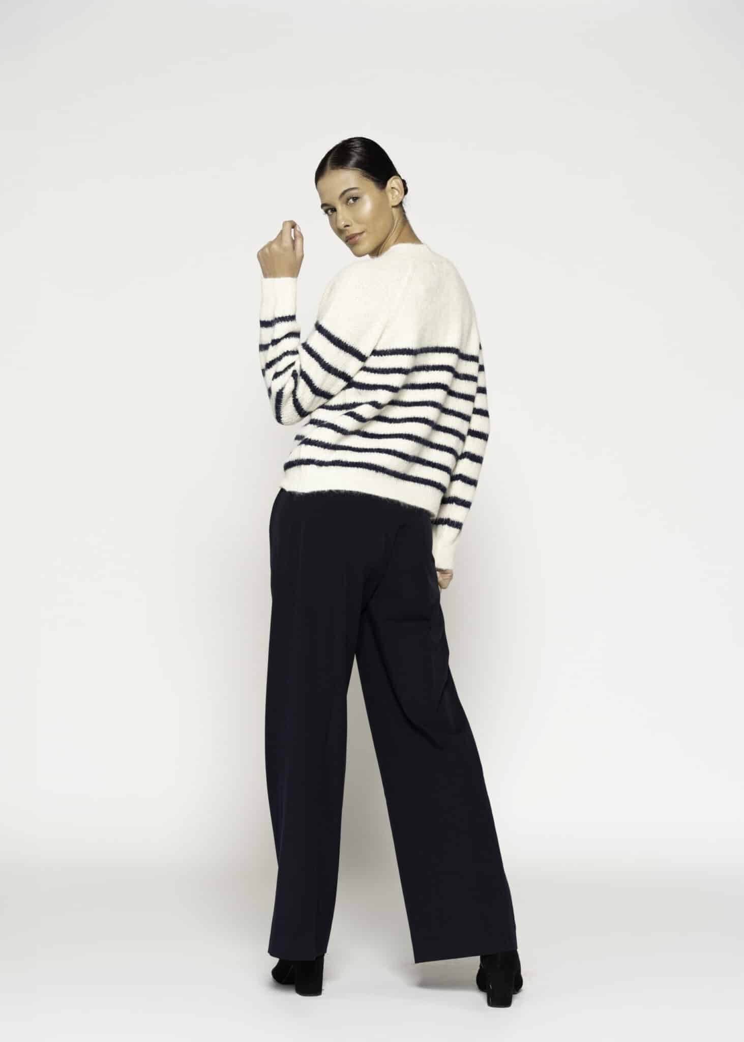 Vista de espalda tres cuartos del sweater tejido a rayas horizontales crudo y azul marino, mostrando caída oversize y pantalones negros amplios