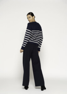 Vista de espalda del sweater a rayas azul marino y blancas, mostrando el ajuste holgado y la caída sobre pantalón negro, modelo Formentera