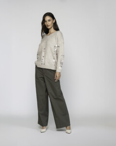 Vista frontal lateral de sweater tejido beige con lentejuelas plateadas en mangas, combinado con pantalón verde oliva y stilettos claros