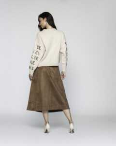 Vista de espalda del sweater beige con letras doradas en mangas y espalda, combinado con falda midi en tonos tierra