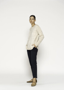 Vista de perfil del sweater beige con motas de colores, tejido de punto con cuello redondo, manga larga y caída amplia sobre pantalón negro