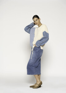 Vista lateral de sweater bicolor crudo y azul con mangas en denim, cordón ajustable visible en el bajo, modelo Formentera