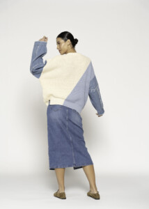 Vista de espalda del sweater bicolor en tejido de punto crudo y azul lavanda, con falda denim midi y calzado beige