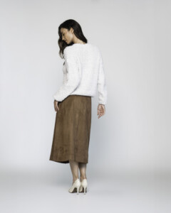 Vista de espalda del sweater blanco textura bouclé con falda marrón, se aprecia el largo y caída del tejido, modelo Formentera