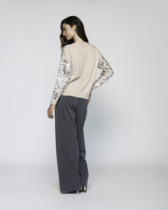 Vista de espalda del sweater beige claro, mangas con lentejuelas plateadas y negras, puños de tejido canalé, pantalón gris ancho