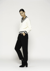 Vista lateral de tres cuartos mostrando sweater tejido crudo con ribetes negros en cuello V y puños, combinado con pantalón negro