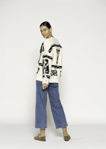 Vista lateral del sweater crudo con diseño gráfico negro en manga y espalda, combinado con pantalón denim azul