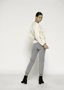 Vista de espalda del sweater tejido crudo mostrando las lentejuelas aplicadas en las mangas, combinado con pantalón gris