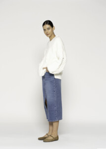Vista lateral de sweater crudo con textura acolchada tipo rombo, cuello en V y mangas amplias, combinado con falda denim azul