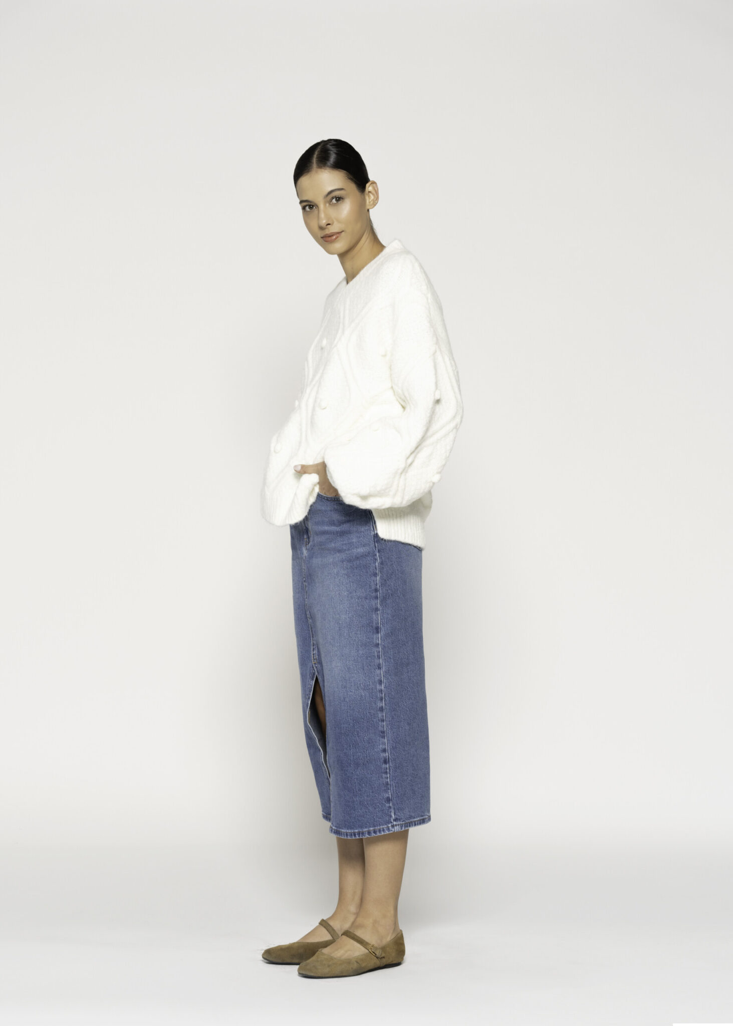 Vista lateral de sweater crudo con textura acolchada tipo rombo, cuello en V y mangas amplias, combinado con falda denim azul