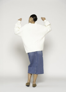 Vista de espalda del sweater crudo con textura acolchada combinado con falda denim, modelo Formentera
