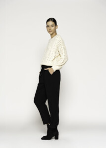 Vista lateral de sweater tejido calado crudo con trenzas y punto abierto, se aprecia la caída del tejido sobre pantalón negro