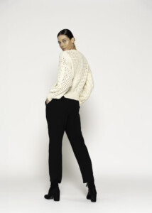 Vista de espalda del sweater crudo tejido calado con trenzas y mangas largas, combinado con pantalón negro y botines