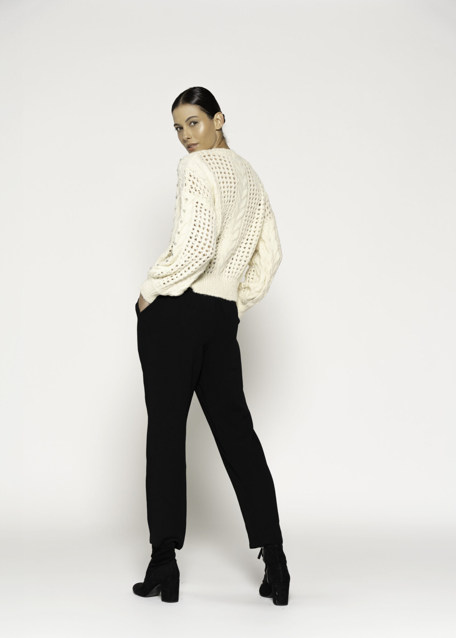Vista de espalda del sweater crudo tejido calado con trenzas y mangas largas, combinado con pantalón negro y botines