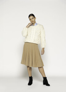 Vista completa de outfit con sweater tejido crudo de trenzas en relieve sobre falda plisada camel y botines negros