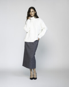 Vista de tres cuartos del sweater blanco de cuello alto con tejido texturado, combinado con falda midi gris