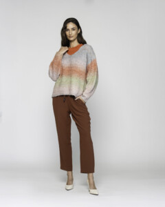 Vista completa de cuerpo entero mostrando sweater degradé con franjas grises, naranjas y verdes, combinado con pantalón marrón chocolate y zapatos blancos, modelo Formentera