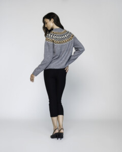 Vista de espalda del sweater gris tejido con guardas geométricas en zigzag beige, negro y blanco sobre los hombros, combinado con pantalón negro