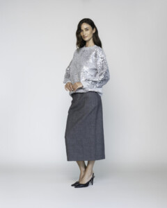 Vista lateral de sweater gris con lentejuelas plateadas en mangas abullonadas, combinado con falda midi gris