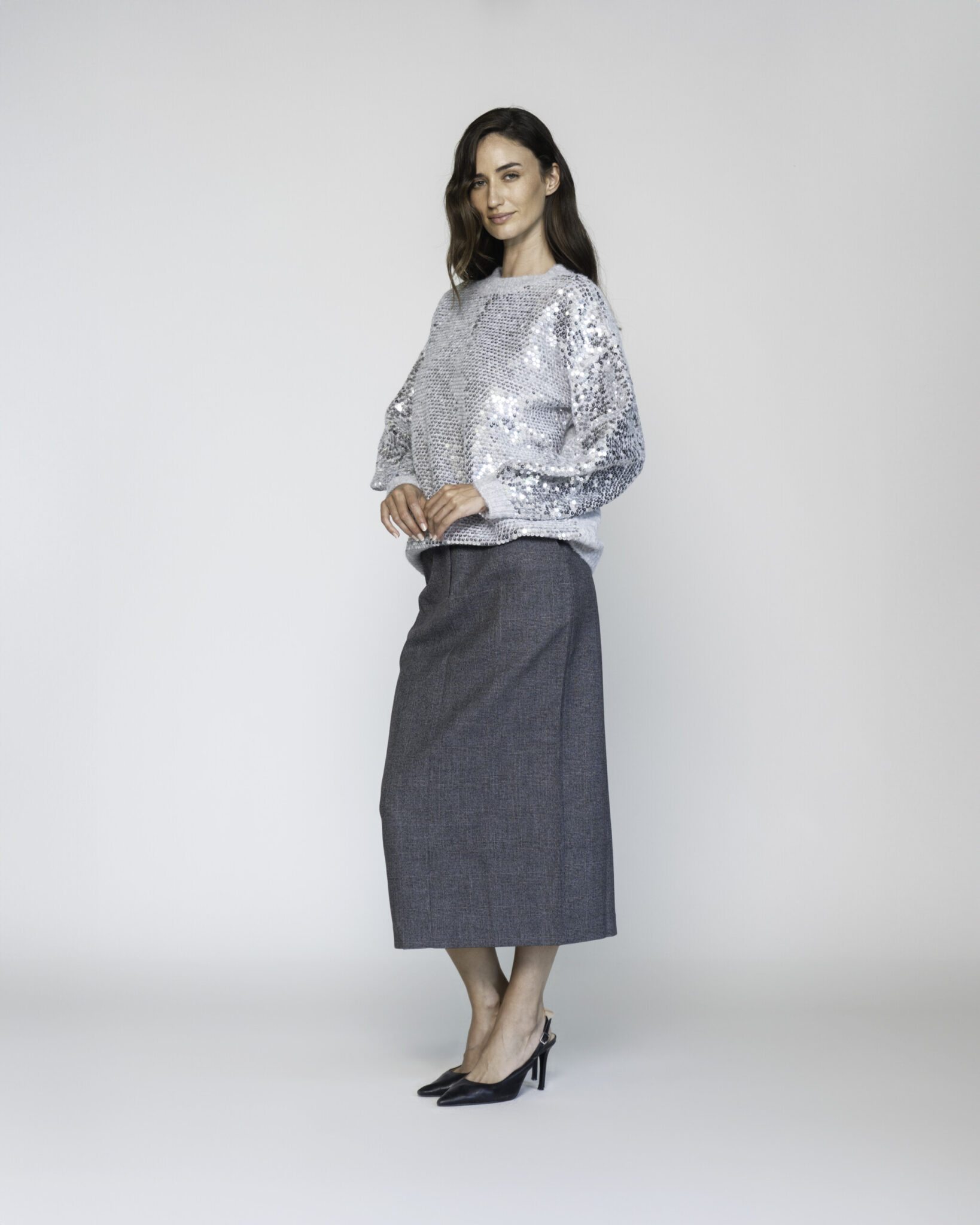 Vista lateral de sweater gris con lentejuelas plateadas en mangas abullonadas, combinado con falda midi gris