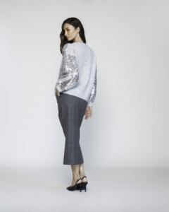 Vista lateral de sweater tejido gris claro con mangas cubiertas de lentejuelas plateadas, combinado con pantalón oscuro