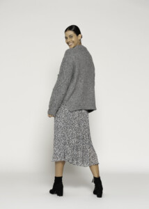 Vista de perfil lateral mostrando sweater gris oversized de tejido grueso combinado con falda estampada de largo midi, modelo Formentera