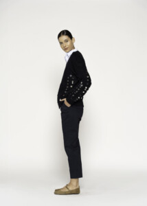 Vista lateral de sweater negro de punto con botones metálicos en las mangas, sobre camisa blanca y pantalón oscuro