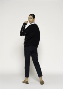 Vista de perfil del sweater negro con detalle de botones metálicos en manga y cuello blanco asomando, modelo Formentera