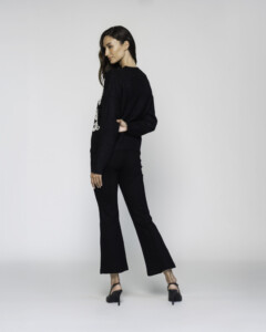 Vista de espalda del sweater negro de punto con manga larga, combinado con pantalón flare negro y sandalias de tacón, modelo Formentera