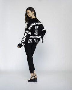 Vista lateral de tres cuartos mostrando la espalda del sweater negro con diseño gráfico blanco en contraste, punto grueso visible