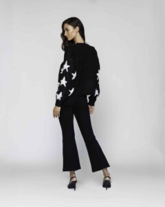 Vista trasera tres cuartos de sweater negro con estrellas blancas en las mangas, combinado con pantalón negro acampanado