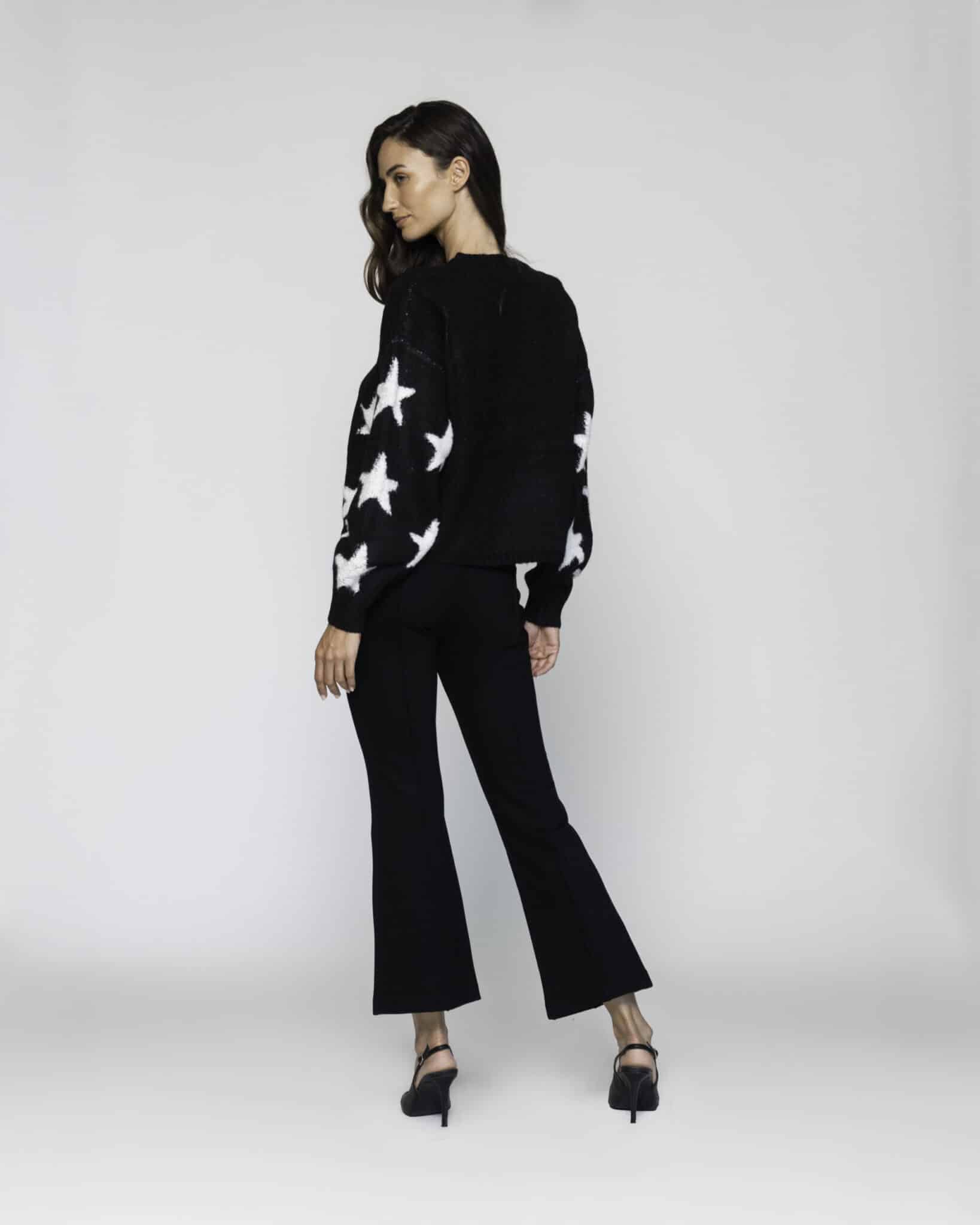 Vista trasera tres cuartos de sweater negro con estrellas blancas en las mangas, combinado con pantalón negro acampanado